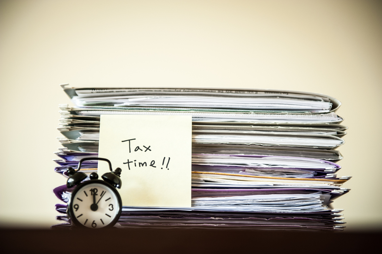 Clock beside a pile of papers with a post it reading Tax Time