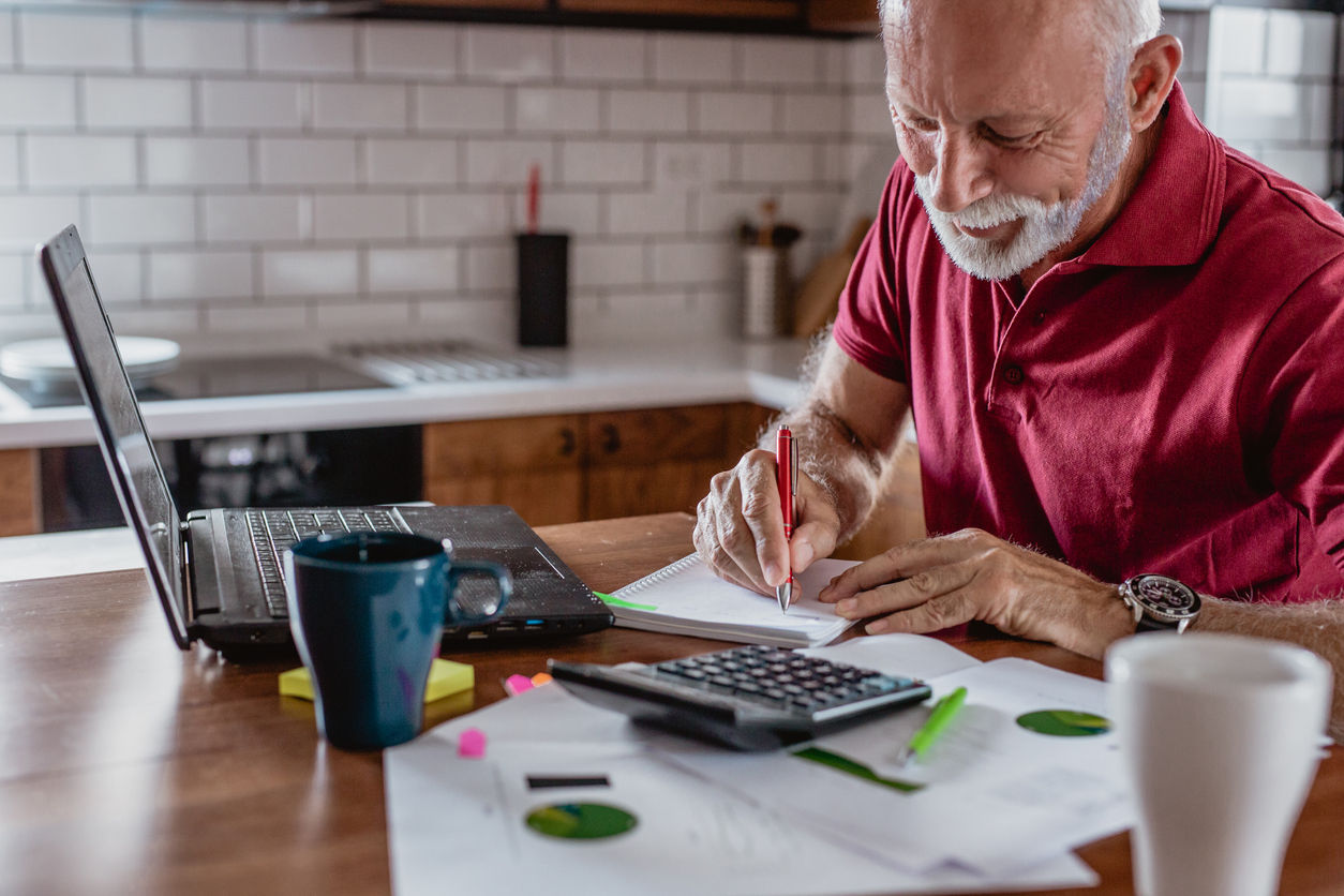 Senior man sitting at table with laptop planning finances