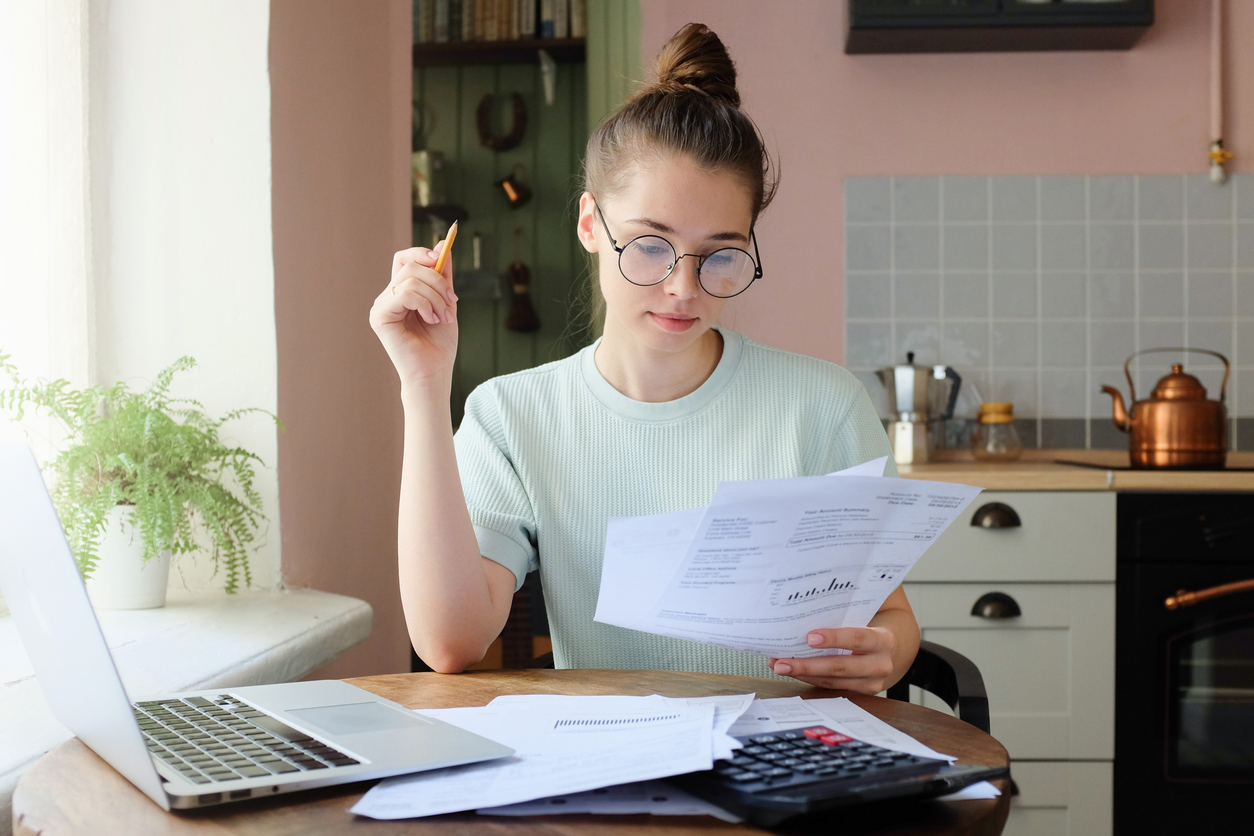 Young woman at table with laptop and documents reviewing her finances