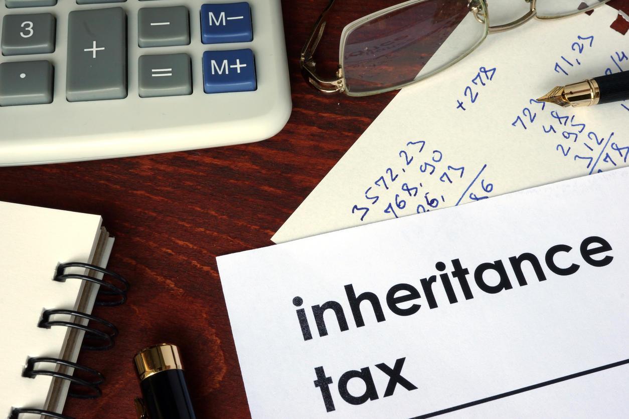 Paper titled inheritance tax on desk with calculator, calculations, and a pair of glasses