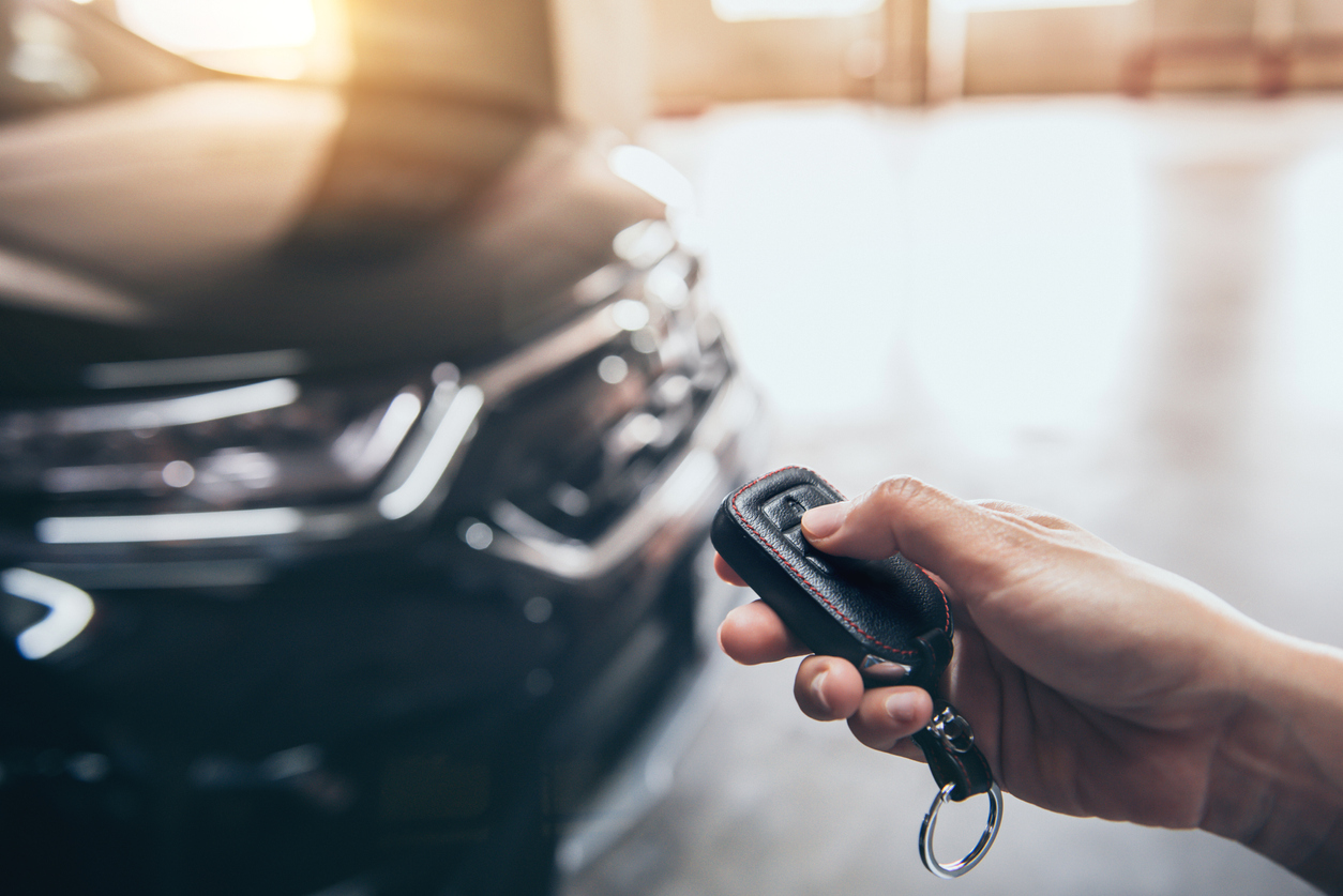 Close up of hand clicking on electronic car key with car in background