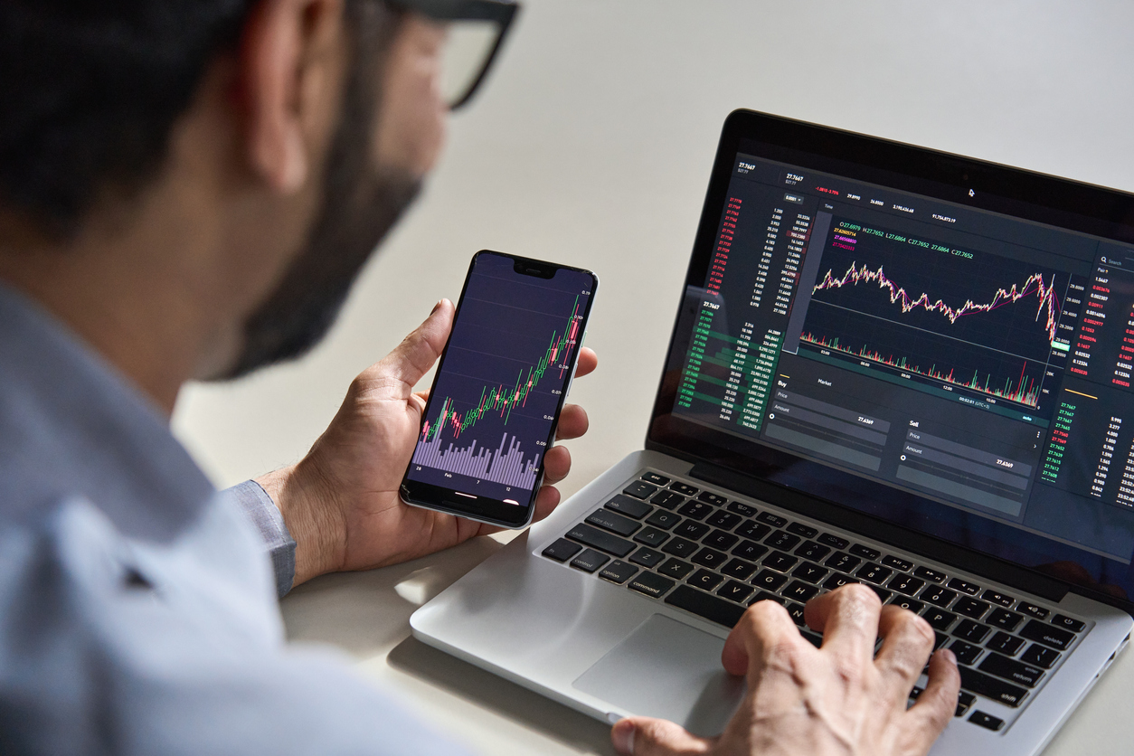 Man looking at stocks and shares on phone and laptop