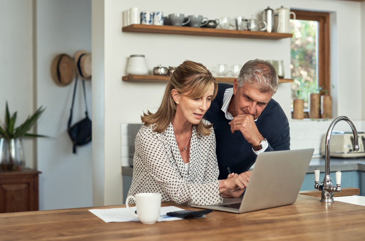 Mature couple in their kitchen reviewing finances on their laptop - Understanding the Lifetime Allowance - the rising cost of retirement