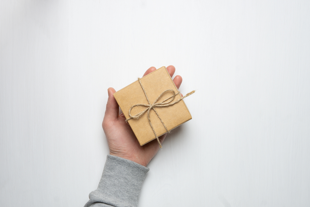 Hand holding gift wrapped in brown paper and tied with a bow representing inheritance gifting
