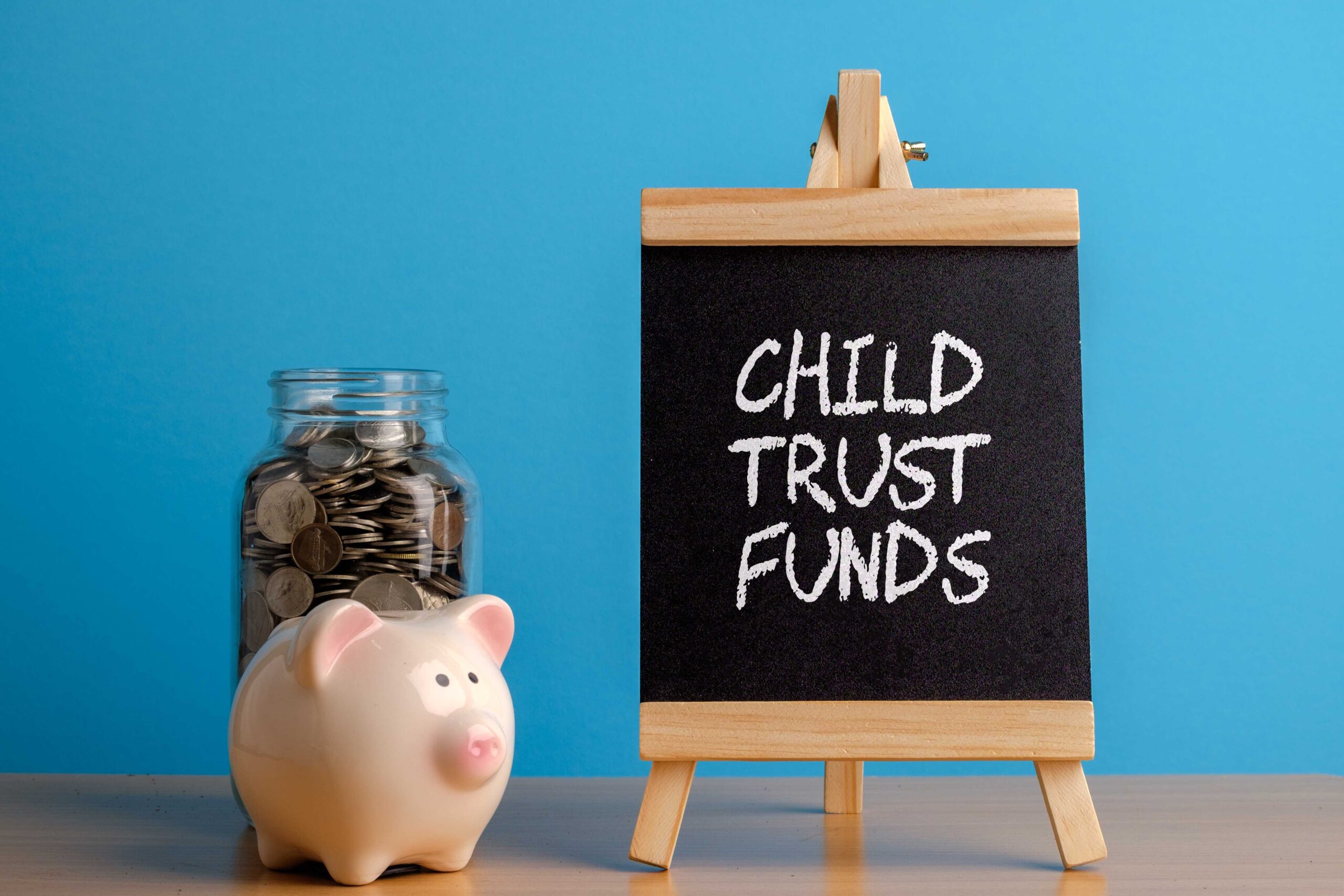 Blackboard with 'Child Trust Fund' written on it alongside a piggy bank and pot of money - £394 million unclaimed in child trust funds