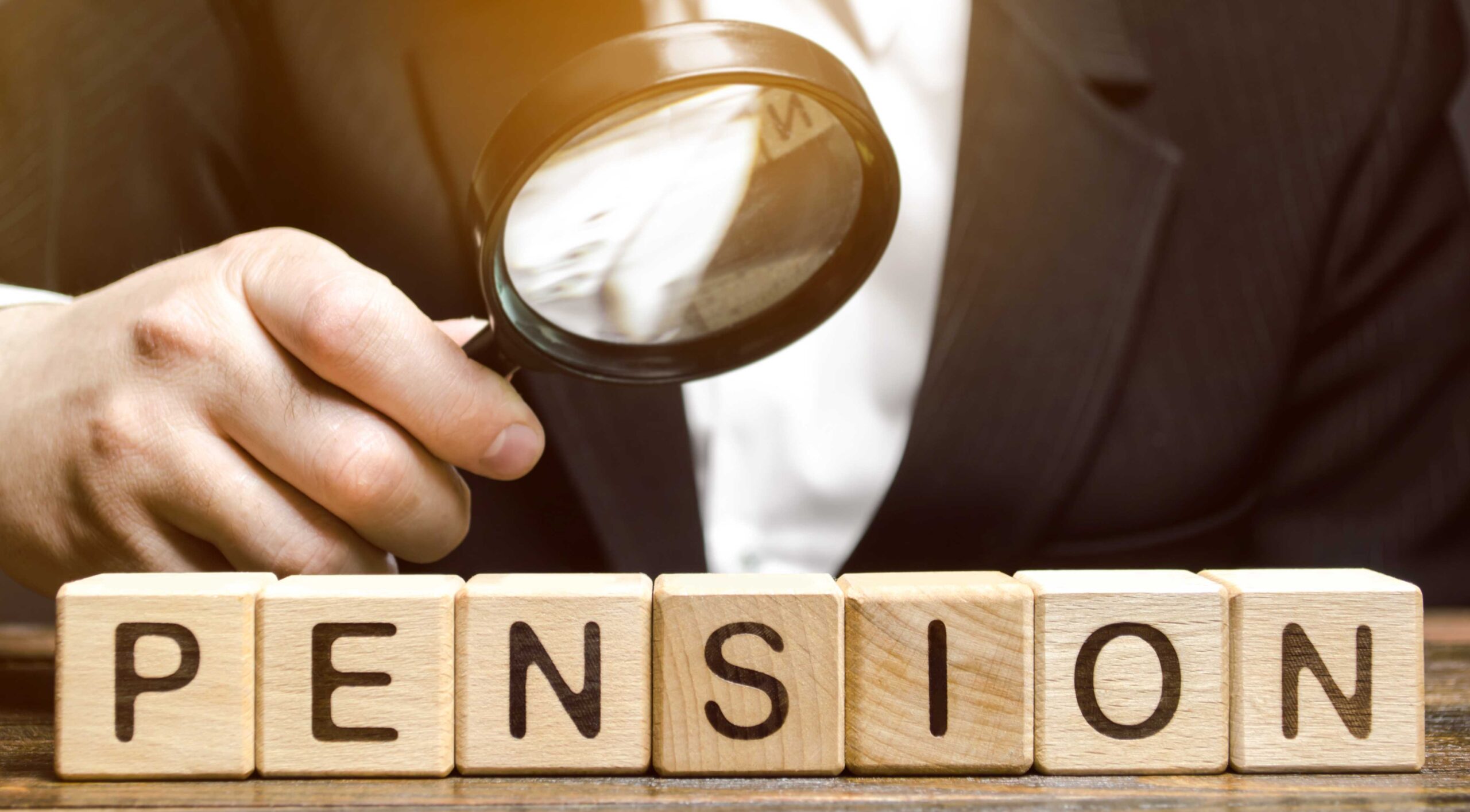 Graphic of a close up of a person in a suit holding a magnifying glass over wooden blocks spelling out the word 'Pension'.